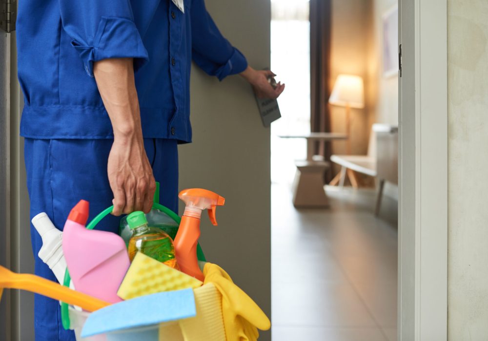 Professional cleaner with bucket of detergents opening room